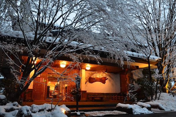 A traditional Japanese-style building with a wooden exterior, a stone entrance, and a snow-covered landscape.