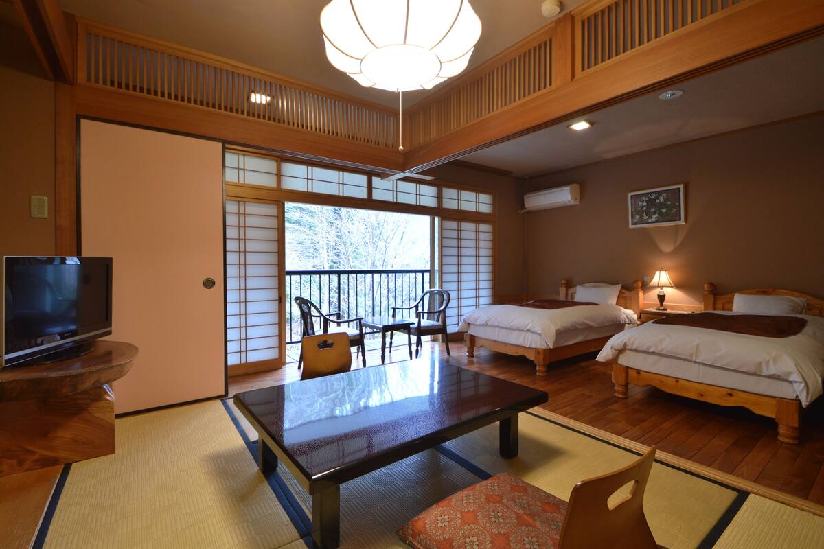 Ein traditioneller japanischer Raum mit Tatami-Boden, einem niedrigen Tisch, zwei Betten und einem Fernseher.