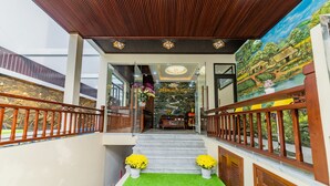 A hotel lobby with a wooden ceiling, a mural, a staircase, and a reception desk. - Green Hill Hotel (Da Nang)