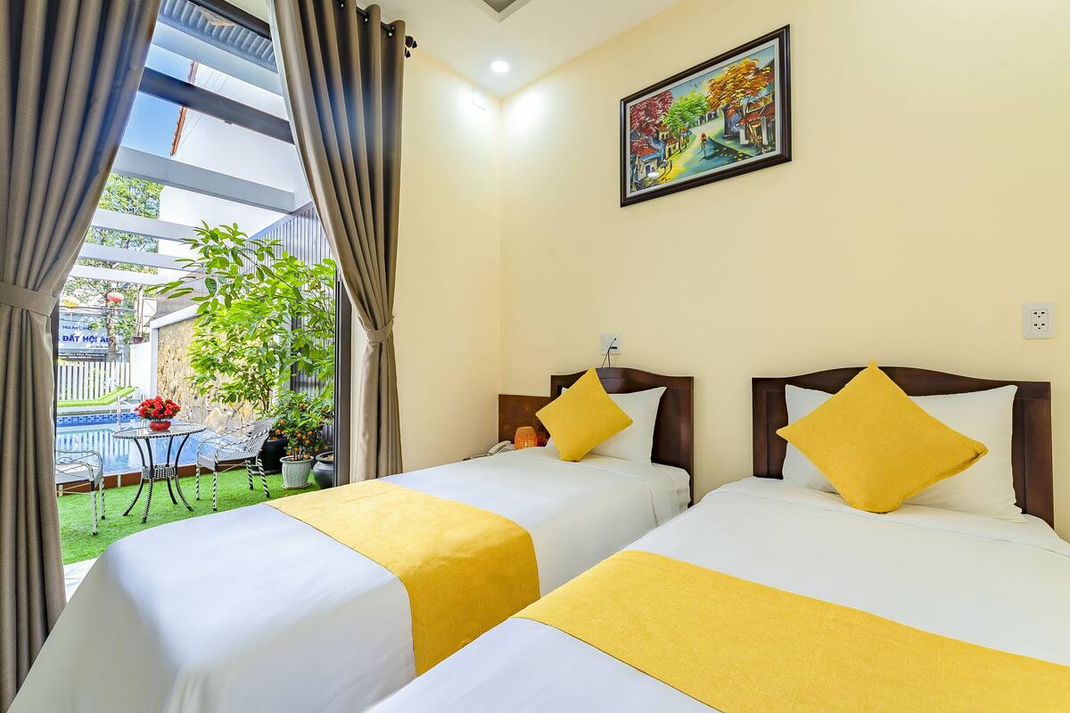 Quarto de hotel com duas camas, um quadro na parede e vista para uma piscina e jardim.