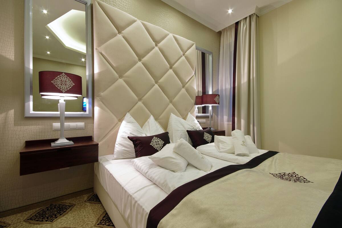 A hotel room with a large bed, a nightstand, a lamp, and a mirror.