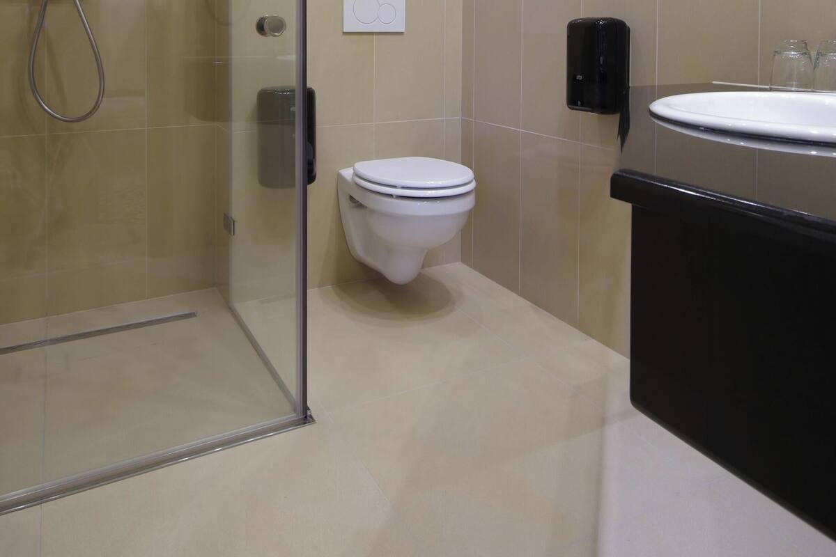 A bathroom with a toilet, a glass shower enclosure, a sink, and a soap dispenser.