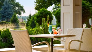 A patio with wicker chairs and a table, a drink with a straw, and a glass of orange juice. - Arcanum Hotel (Bekescsaba)
