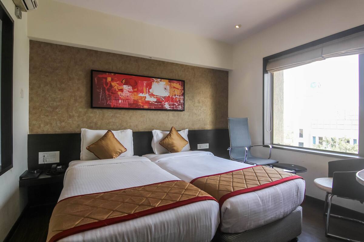 A hotel room with two beds, a large window, a desk, and a chair.