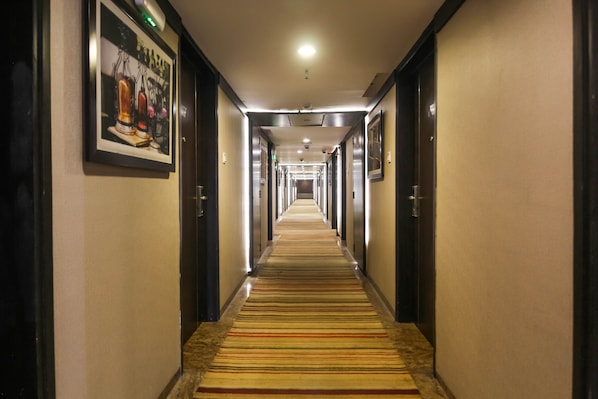 A hotel hallway with a striped carpet, framed artwork on the walls, and doors leading to rooms.