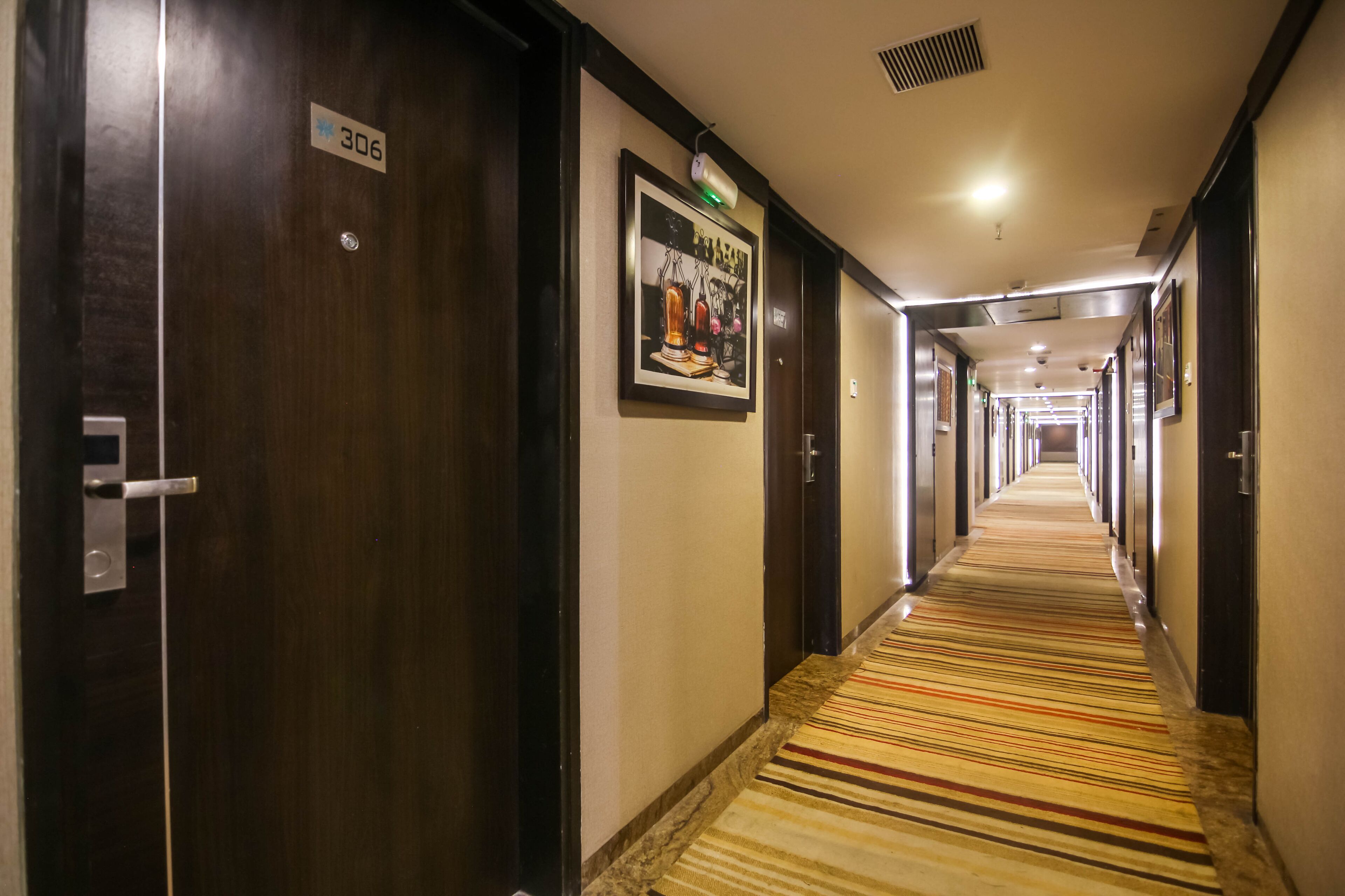 A hotel hallway with a striped carpet, wooden doors, and a framed picture on the wall.