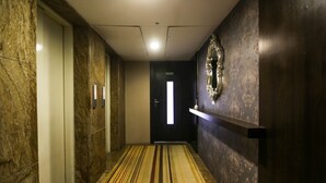En hall med ett randigt golv, en dörr med en skylt som visar utgången i nödfall och en dekorativ detalj som hänger på väggen.