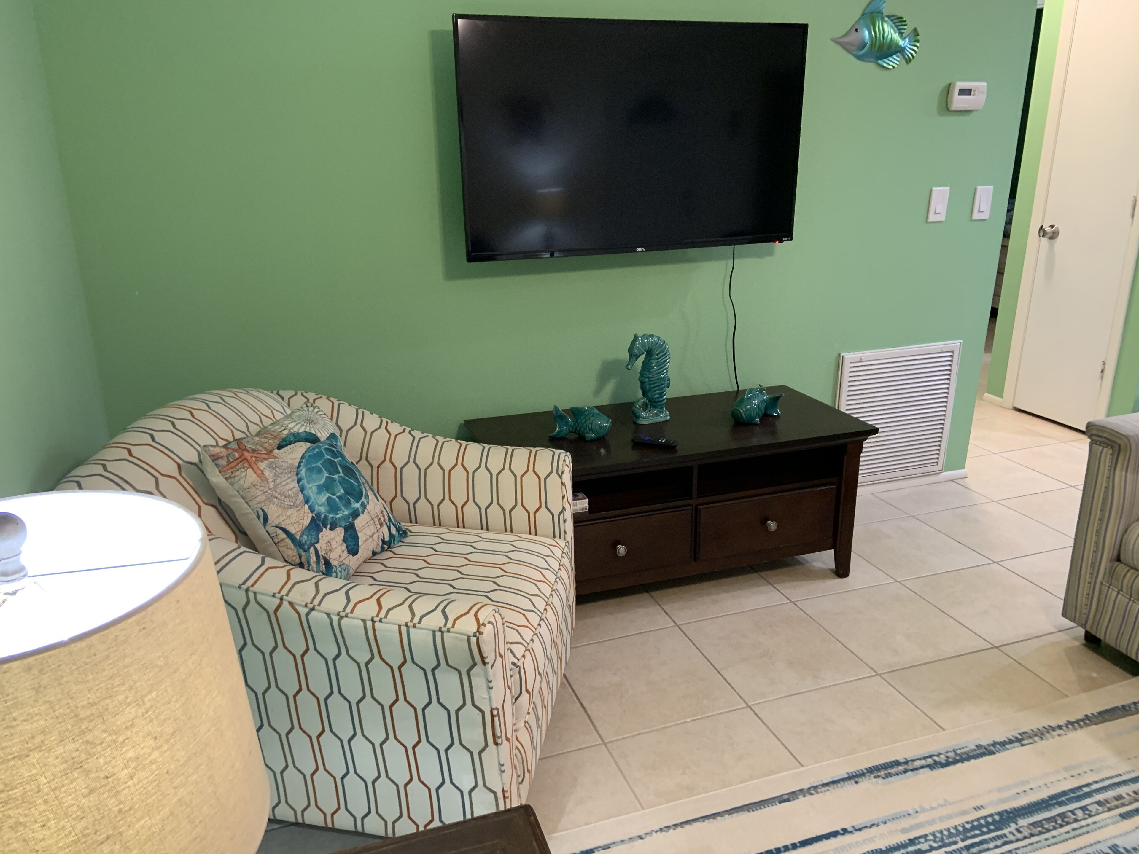 Una sala de estar con un sofá, un televisor montado en la pared y objetos decorativos sobre una mesa.