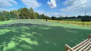 Un court de tennis avec un filet, entouré d’arbres et d’une clôture.
