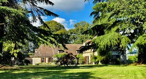 A traditional stone building with a water wheel, surrounded by lush greenery and trees.