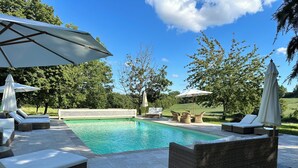 Une piscine entourée de verdure, avec des chaises longues et des parasols.