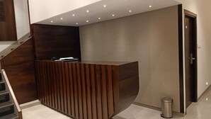 A modern reception desk with a wooden finish, a staircase to the left, and a door to the right. - Hotel Flora Suites (Mumbai)