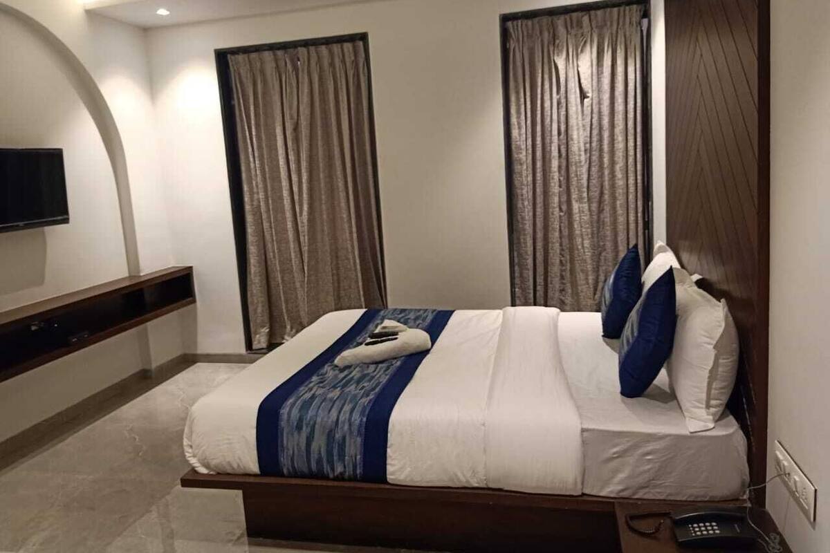 A modern bedroom with a large bed, dark wood headboard, and a flat-screen TV mounted on the wall.