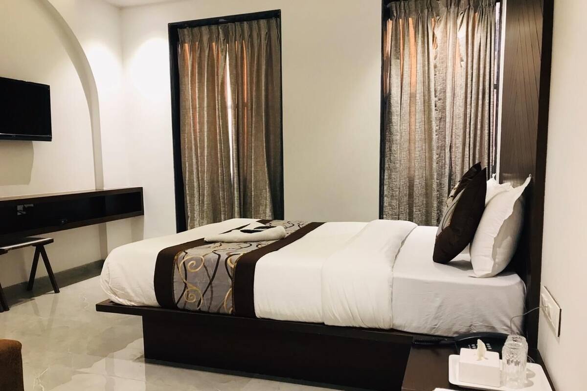 A modern hotel room with a large bed, a flat-screen TV mounted on the wall, and a bedside table with a lamp and a tissue box.
