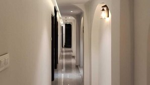 A long, narrow hallway with a polished floor, recessed lighting, and a wall-mounted light fixture. - Hotel Flora Suites (Mumbai)