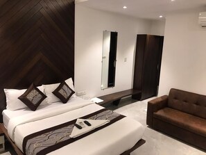 A modern hotel room with a large bed, a sofa, a mirror, and a bench. - Hotel Flora Suites (Mumbai)