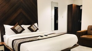 A modern bedroom with a wooden headboard, a large bed with white bedding, a brown sofa, and a mirror on the wall. - Hotel Flora Suites (Mumbai)