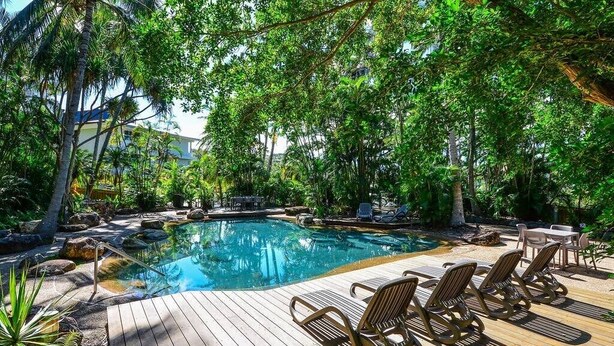 A pool with lounge chairs and a wooden deck surrounded by lush greenery. - Poinciana Lodge 111, Seaview Apartment on Hamilton Island (Hamilton Island)