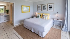 A bedroom with a bed, bedside tables, a nightstand, a ceiling fan, and framed pictures on the wall. - Poinciana Lodge 111, Seaview Apartment on Hamilton Island (Hamilton Island)