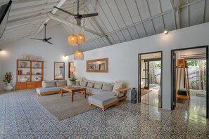 A spacious living area with a large sofa set, a coffee table, and a wooden side table. There are two ceiling fans, a hanging light fixture, and a large mirror on the wall. - 10-bedroom private estate in Seminyak, perfect for large groups, family gatherings, retreats, and celebrations. Enjoy daily breakfast, a private chef, airport transfers, complimentary massages, housekeeping, and a dedicated driver. (Seminyak)