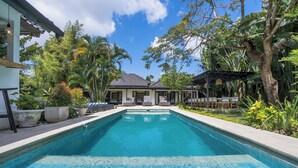 A swimming pool with lounge chairs and umbrellas, surrounded by tropical plants and a building with a tiled roof. - 10-bedroom private estate in Seminyak, perfect for large groups, family gatherings, retreats, and celebrations. Enjoy daily breakfast, a private chef, airport transfers, complimentary massages, housekeeping, and a dedicated driver. (Seminyak)