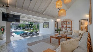 A modern living room with a flat-screen TV, a pool, and outdoor seating. - 10-bedroom private estate in Seminyak, perfect for large groups, family gatherings, retreats, and celebrations. Enjoy daily breakfast, a private chef, airport transfers, complimentary massages, housekeeping, and a dedicated driver. (Seminyak)