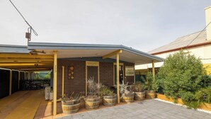 A building with a covered entrance, a brick wall, and a sign indicating a restaurant. There are wooden barrels and plants in front. - Flinders Ranges Bed and Breakfast (HAWKER)