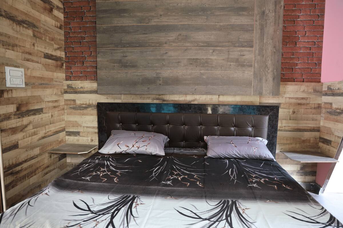 Un dormitorio con cama, dos almohadas, cabecera y pared de ladrillo.