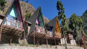 A row of triangular-shaped cabins with balconies, set against a hilly backdrop. - Rakatal Rocks Resort (Lansdowne)