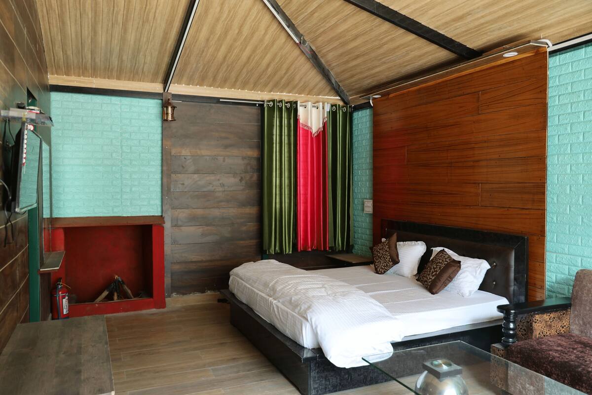 Un dormitorio moderno con techo de madera, una cama con ropa blanca, una mesita de vidrio y una chimenea roja.