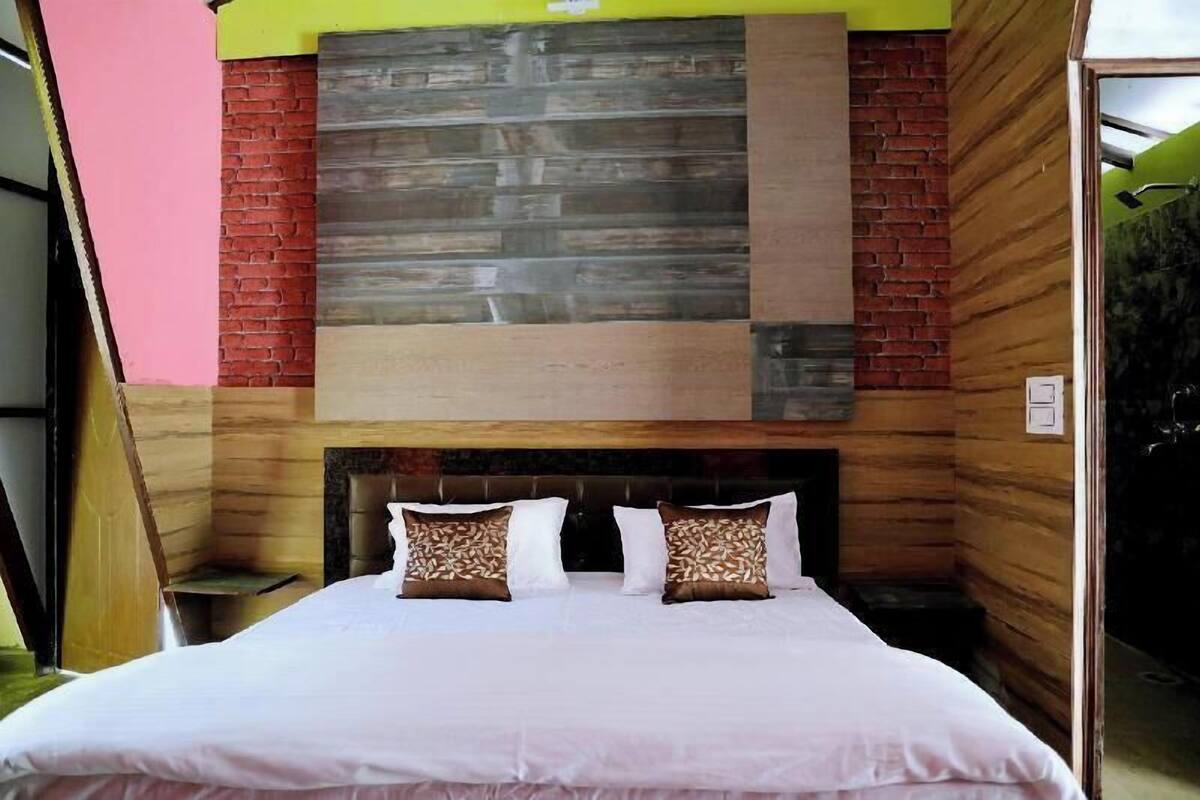Un dormitorio con cama, almohadas, cabecera y pared con diseño de paneles de madera y ladrillo.