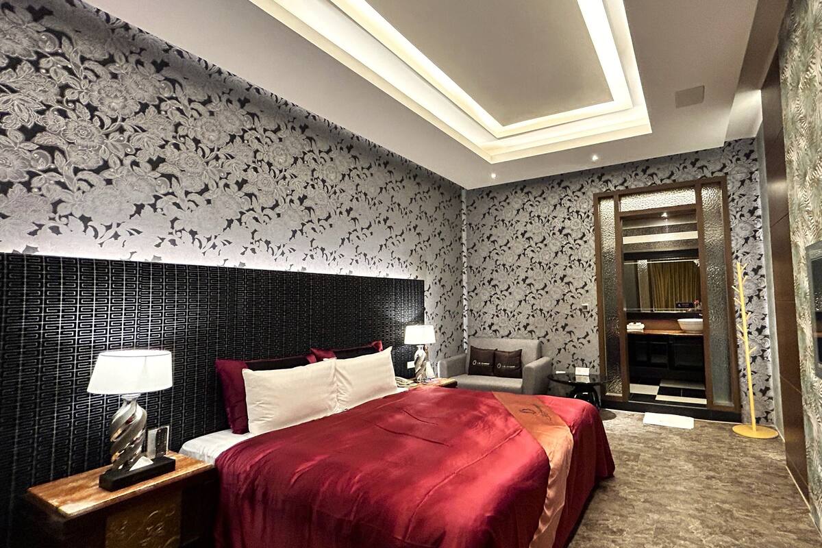 A hotel room with a bed, a nightstand, a TV, and a bathroom visible through an open door.