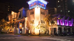A hotel with a prominent tower and illuminated signage, surrounded by palm trees and a street view. - Shining Motel (Taichung)
