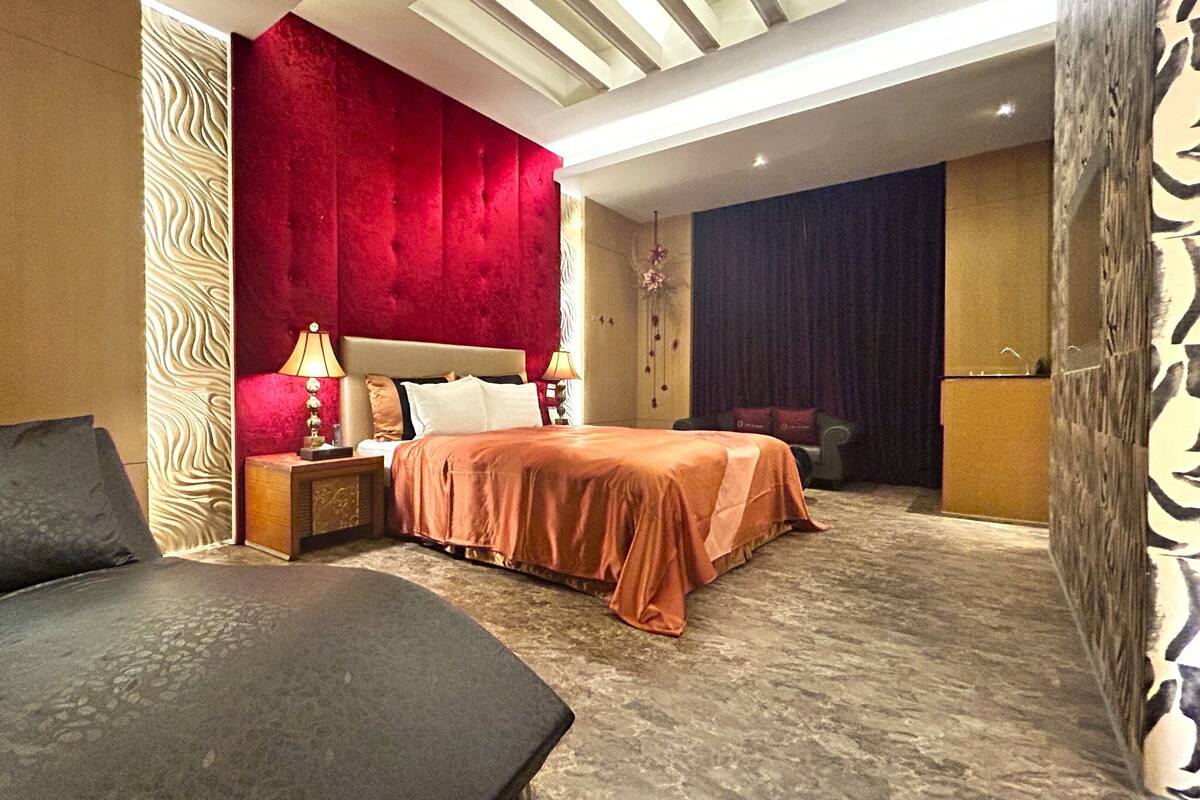 A hotel room with a bed, two bedside tables, a nightstand, a sofa, and a patterned wall.