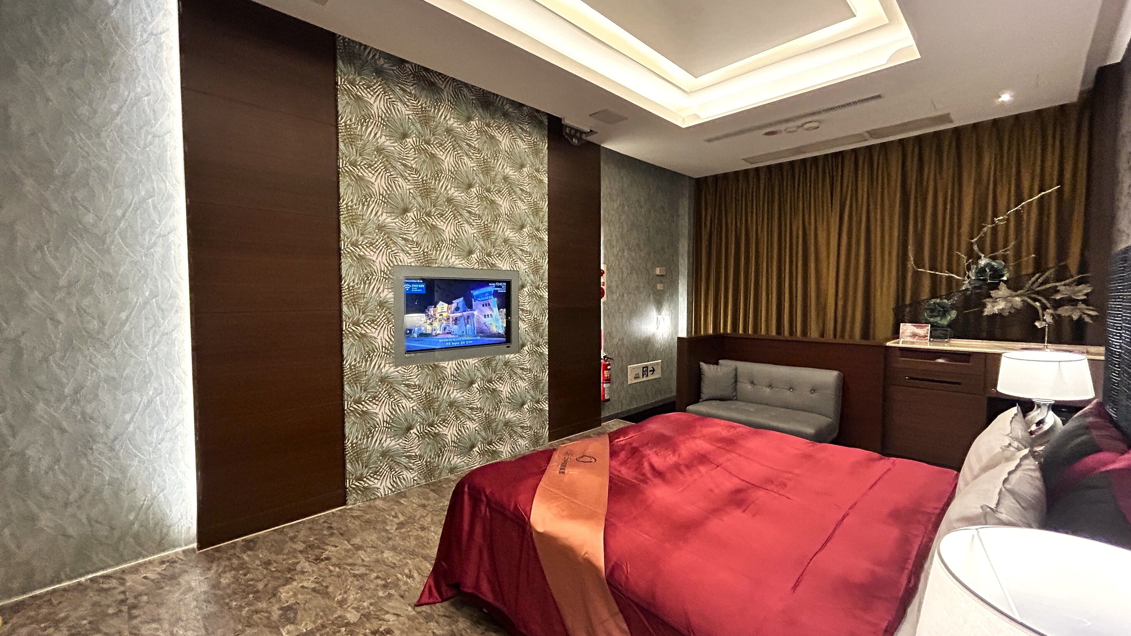A modern hotel room with a large bed, a television mounted on the wall, a bedside table, and a lamp.