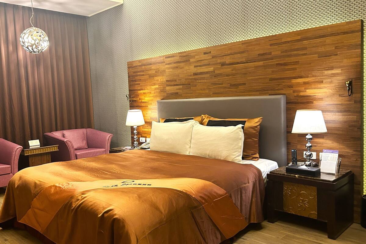 A hotel room with a large bed, two bedside tables with lamps, a desk, and a chair.