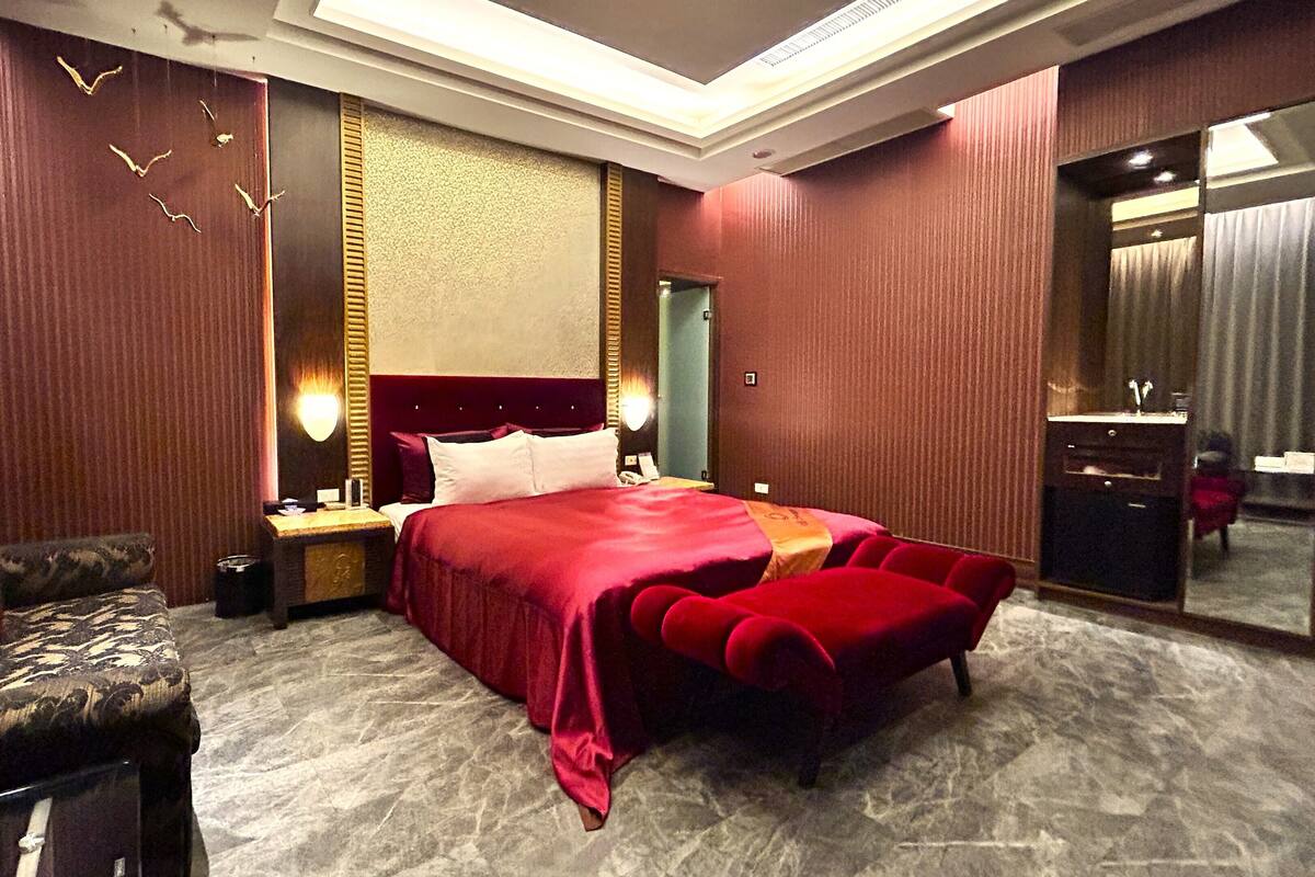 A hotel room with a large bed, a sitting area with a sofa, a vanity with a mirror, and a large window.