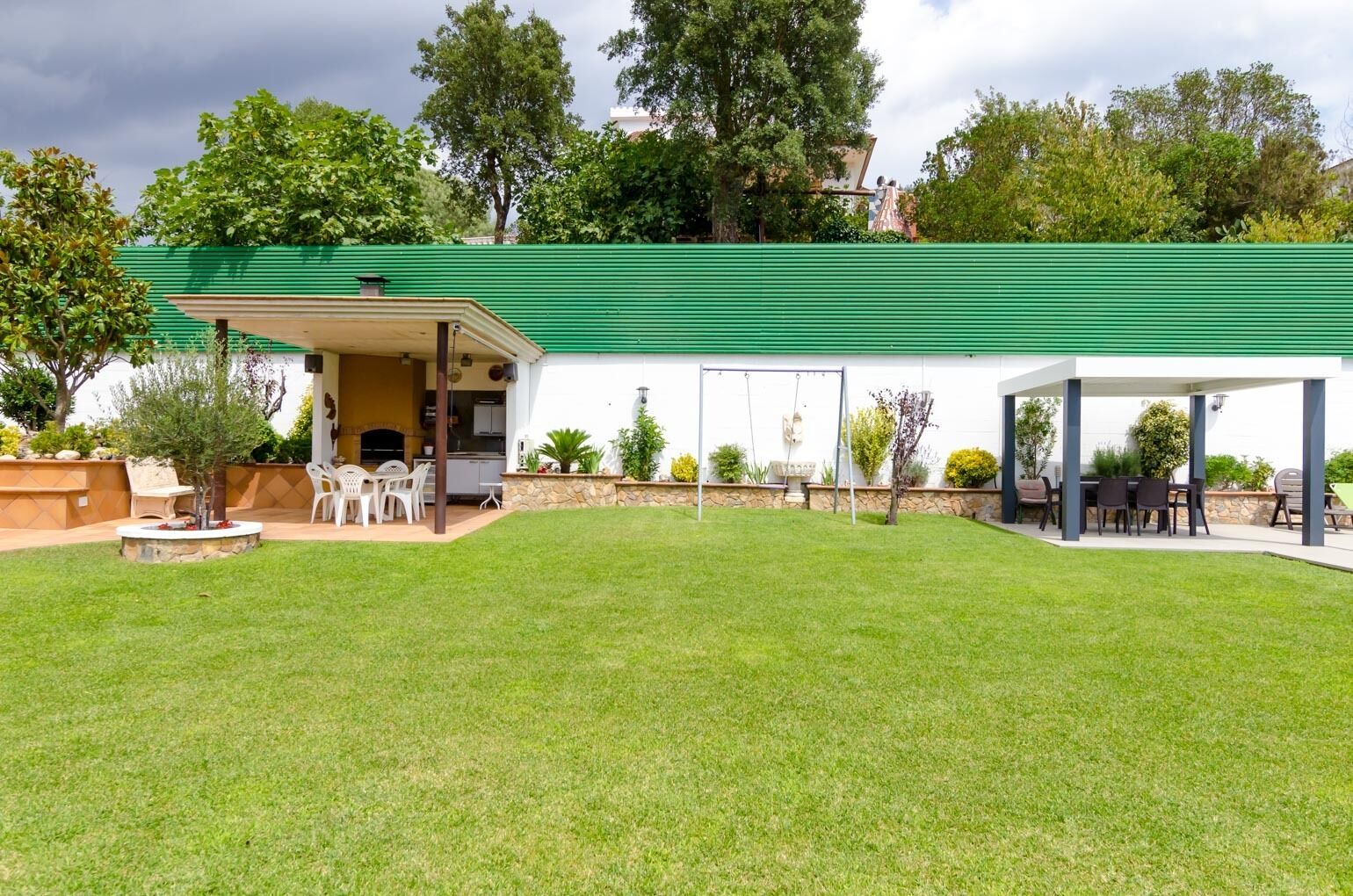 Ein Haus mit überdachter Terrasse, Grillplatz und gepflegtem Rasen.