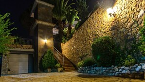 Un edificio de paredes de piedra con una escalera que lleva al segundo piso, un garaje y una entrada bien iluminada.
