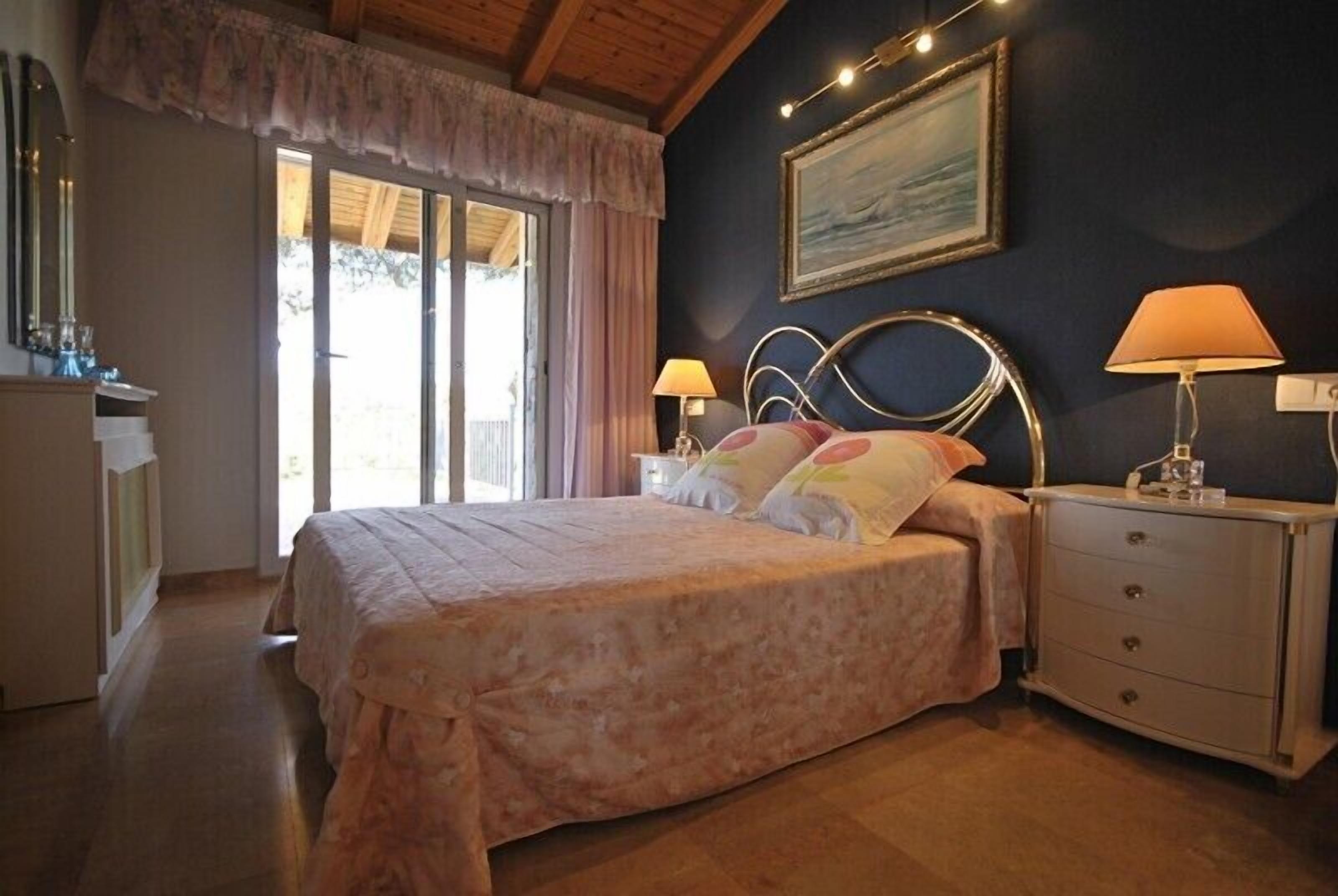Une chambre à coucher avec un lit, deux tables de chevet, une commode, un tableau au mur et une fenêtre avec des rideaux.