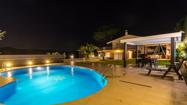 Una piscina con una zona de estar hundida y un porche cubierto con mobiliario exterior.