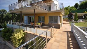 Una casa de dos pisos con balcón, zona de estar al aire libre y un jardín bien cuidado.