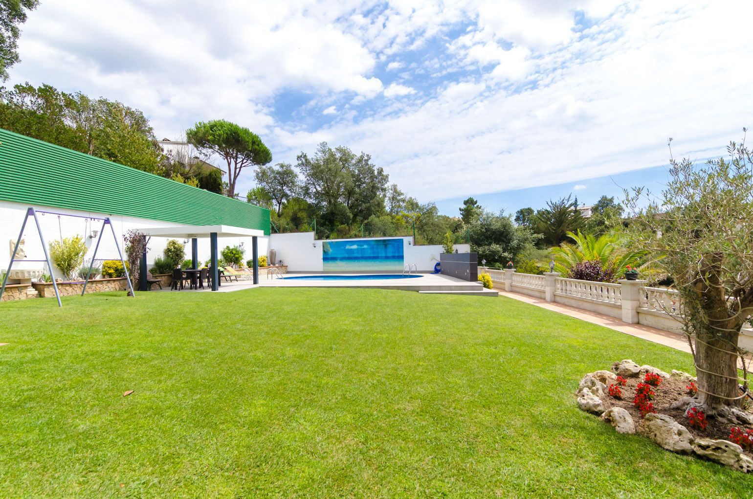 A backyard with a swimming pool, a covered patio, and a well-maintained lawn.