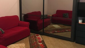 Una habitación con sofá rojo, armario espejado y alfombra estampada.