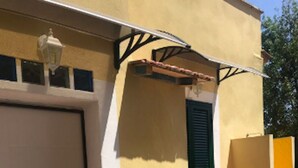 Un edificio con una puerta blanca cerrada, una ventana con contraventanas verdes y una pared amarilla.