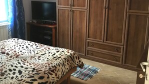 Un dormitorio con una cama, un armario, un televisor y una ventana con cortinas.