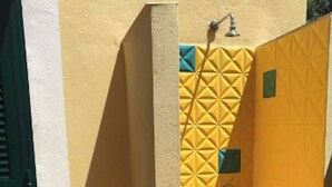 Un espacio de ducha pequeño y cerrado, con una pared amarilla con textura y un balde azul.