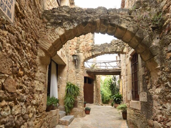 A stone courtyard with an archway, potted plants, and a rustic stone wall. - Green garden & house Pals Beach by Interhome (Pals)