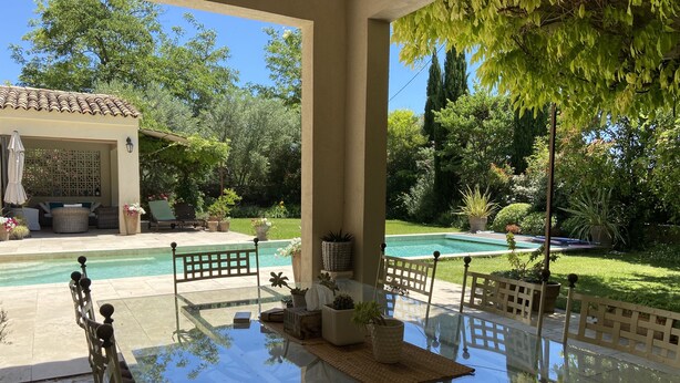 Un patio con paredes de vidrio, una piscina, mobiliario exterior y vistas a un jardín exuberante.