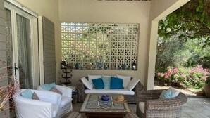 Un patio exterior con mobiliario de mimbre, un sofá blanco y una pared decorativa.